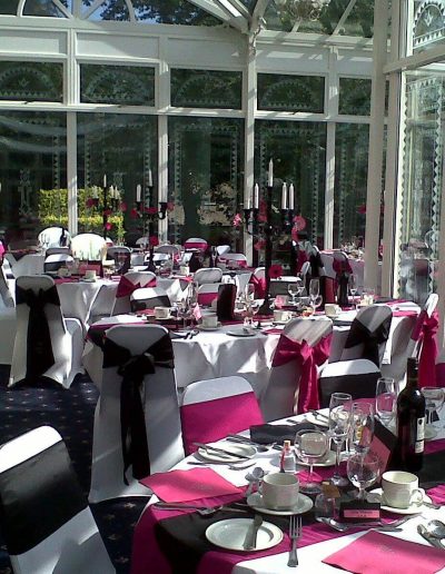 white chair and white table cloth cover, with pink and black sash ribbon bows. The table has a black candle light holder centrepiece.